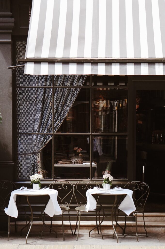 Two bistro table sets on the sidewalk outside of a cafe